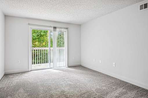 A room with a carpeted floor and a sliding glass door leading to a balcony.