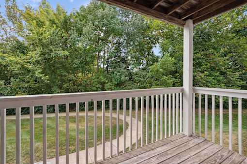 A wooden deck with a white railing overlooks a grassy area.