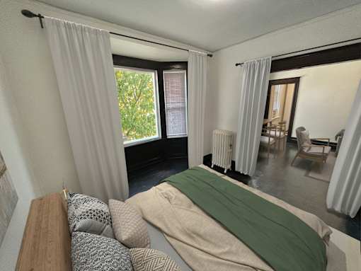 A bedroom with a bed covered in a green blanket and pillows on a wooden headboard.