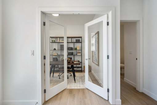 A white door opens to a room with a desk and chairs.