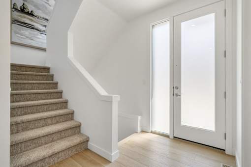 A staircase with a carpeted runner and a white wall.