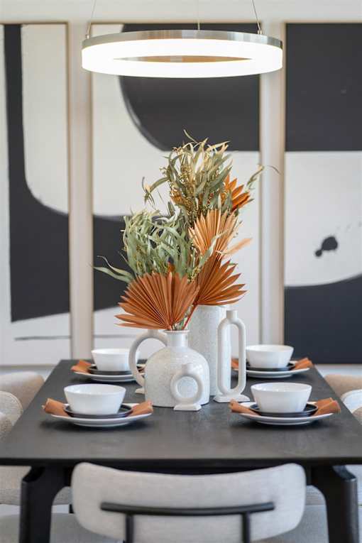 A table with a vase of dried flowers and cups on it.