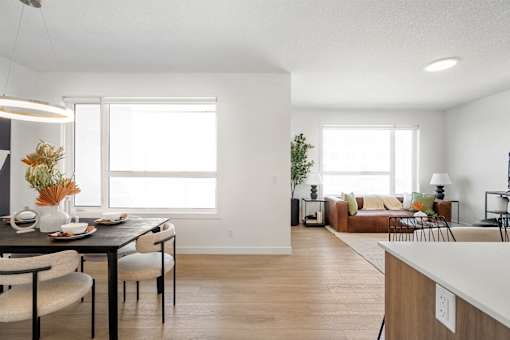 A modern dining room with a table set for two and a couch in the background.