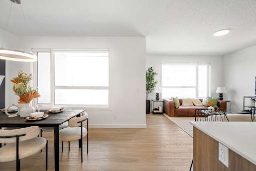 A modern dining room with a table set for two and a couch in the background.