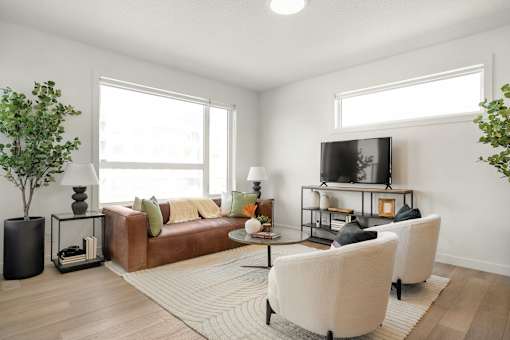 A living room with a brown couch, a white chair, and a television on a stand.