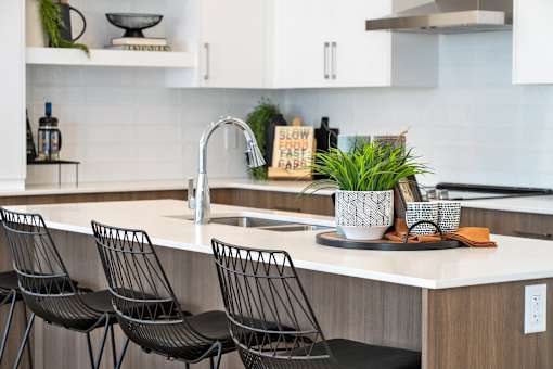 A kitchen with a white countertop and black chairs.