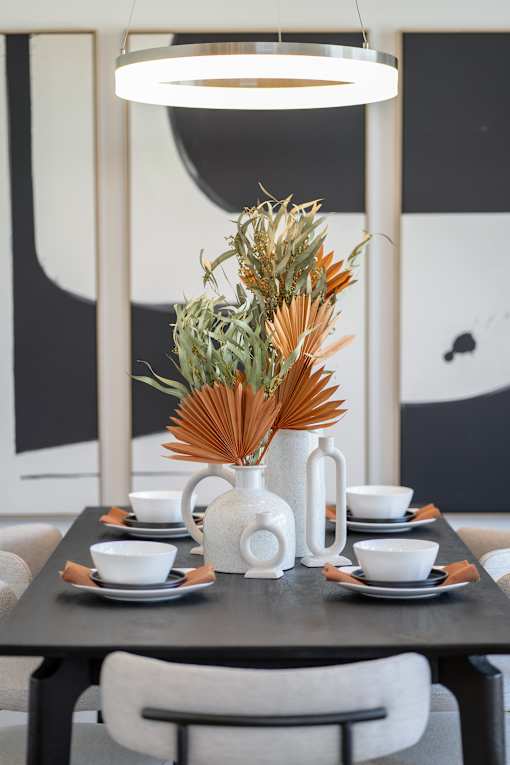 A table set for a meal with a vase of dried flowers as the centerpiece.