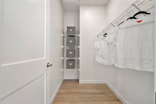 A white closet with clothes hanging and shelves with boxes.