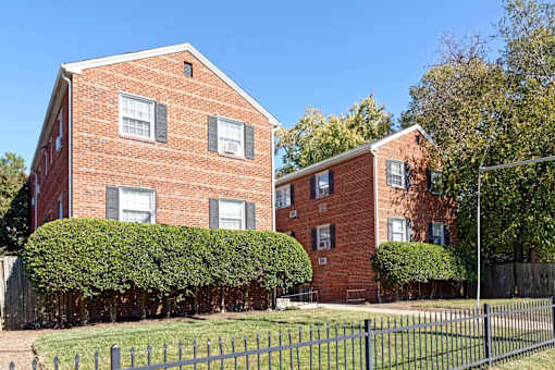 Two red brick houses with green hedges in front.