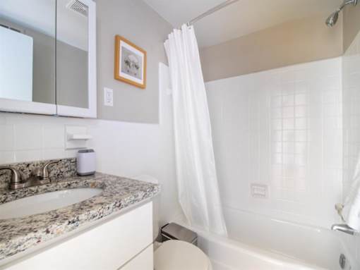 A white bathroom with a stone countertop and a white bathtub.