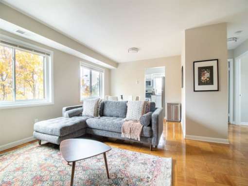 A grey couch with a throw is in a room with a wooden floor and a large window.