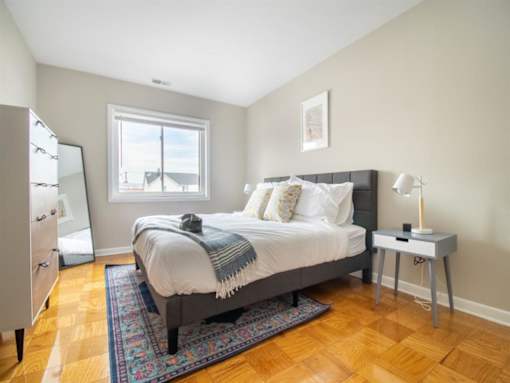 A bedroom with a bed, nightstand, and a window.