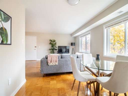 A living room with a grey couch, a glass table, and a white dining table.