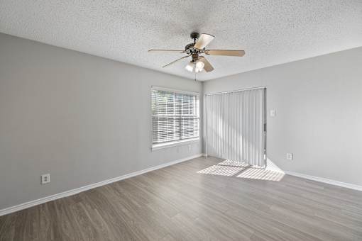 A room with a ceiling fan and light, wooden floors, and a window with blinds.