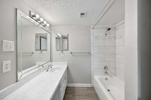 A white bathroom with a sink, mirror, and bathtub.