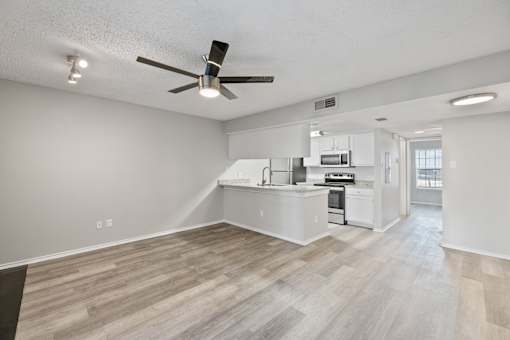 A spacious kitchen and living room with a ceiling fan and lighting fixture.