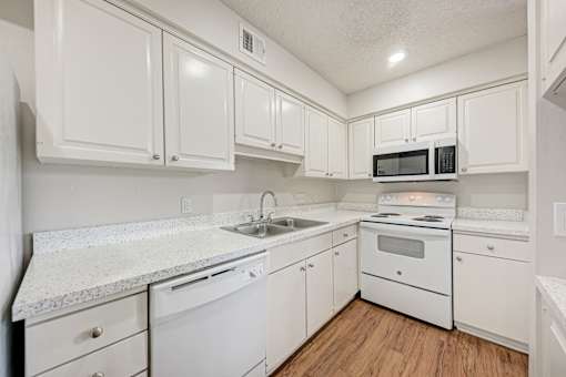 A white kitchen with wood floors and white appliances.