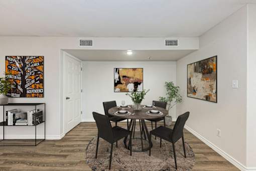 A dining room with a table set for two and a plant on the side table.