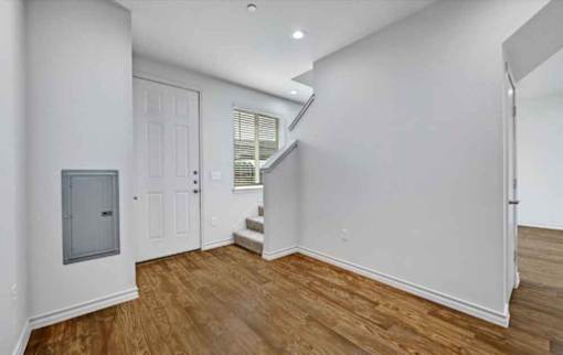 A room with wooden floors and white walls, featuring a white door and a staircase.