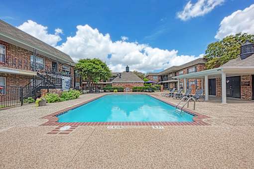 A swimming pool surrounded by a brick building and trees.