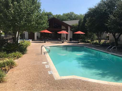 A pool surrounded by trees and umbrellas.