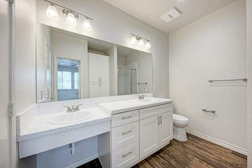 A white bathroom with a double sink and a toilet.