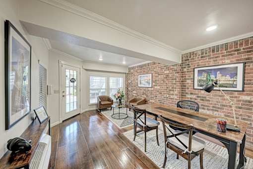 A room with a wooden table and chairs, a brick wall, and a painting of a cityscape.