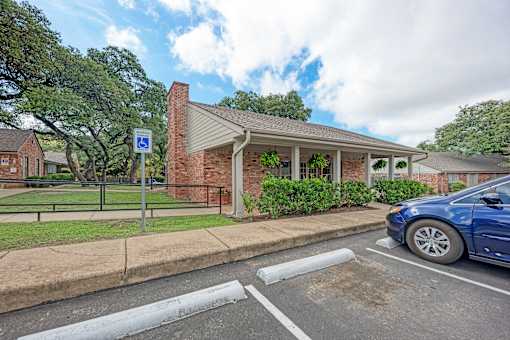 A blue car is parked in a parking space next to a building with a covered porch.