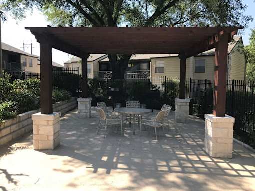 A patio with a table and chairs under a wooden pergola.