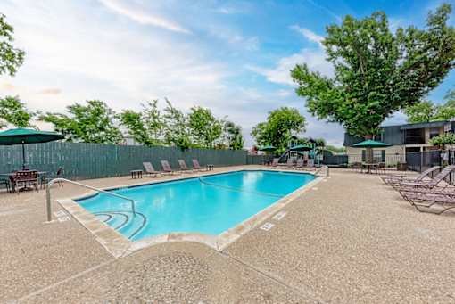 A large outdoor swimming pool surrounded by a fence and lounge chairs.