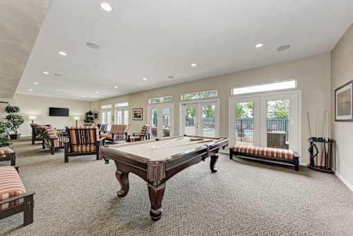 A billiard table is in the middle of a room with striped couches and a television.