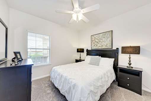 A bedroom with a bed, nightstand, and a ceiling fan.