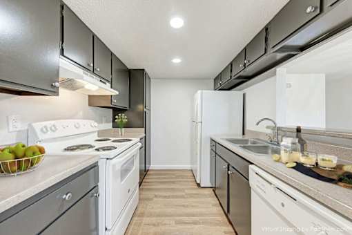 A kitchen with white appliances and a bowl of green apples on the counter.
