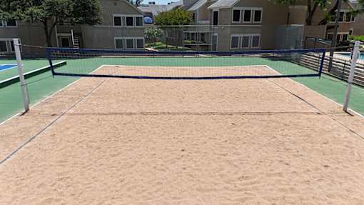 A sand volleyball court with a green fence around it.