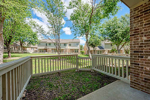 A view from a balcony overlooking a grassy area with trees and houses in the distance.