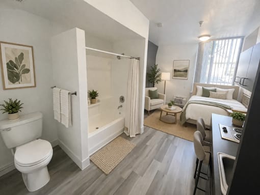 A modern bathroom with a white toilet, a bathtub with a shower curtain, a bed, and a desk with a computer.