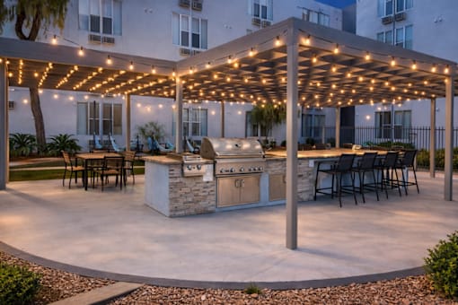 A patio with a barbecue and chairs under string lights.