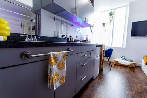 A kitchen with a black counter top and a yellow towel hanging on the handle of a cabinet.