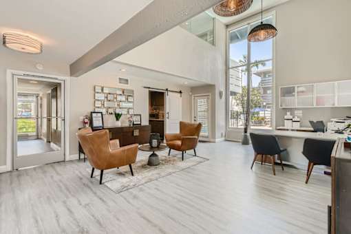 A modern living room with a large window and a kitchen area in the background.