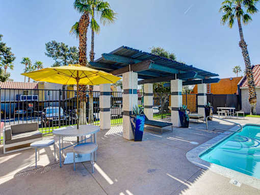 A pool area with a yellow umbrella and a table.
