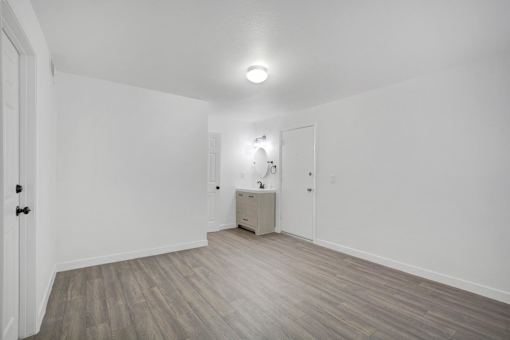 A room with a wooden floor and a white wall with a cabinet and a mirror.