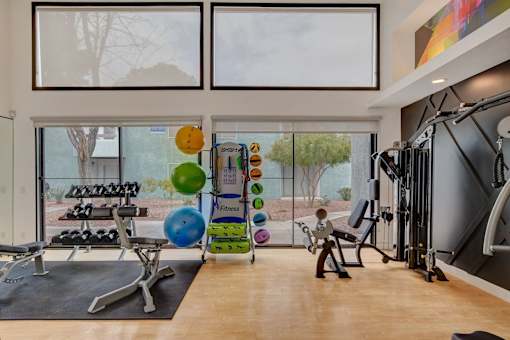 A gym with a variety of equipment and a view of trees outside the window.