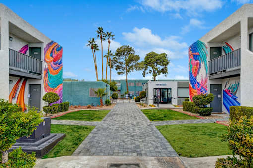 A walkway leads between two buildings with colorful murals on the walls.