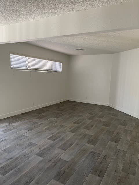 A room with a wooden floor and a window with blinds.