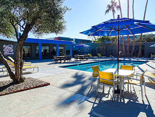 A pool area with a blue umbrella and yellow chairs.