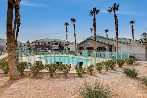 A pool surrounded by palm trees and a building in the background.