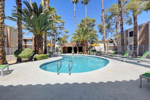 A pool surrounded by palm trees and lounge chairs.