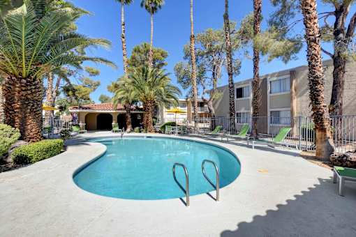 A pool surrounded by palm trees and a building in the background.