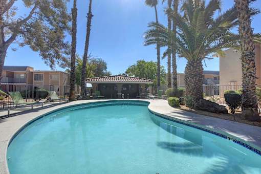 A swimming pool surrounded by palm trees and a building in the background.