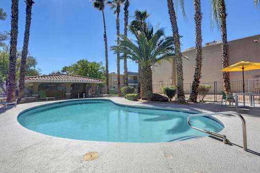 A pool surrounded by palm trees and a building in the background.